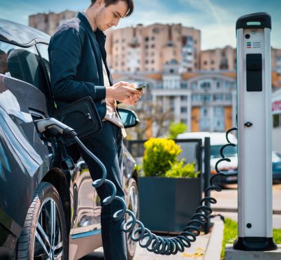 Man charging his electric car at charge station and using smartphone