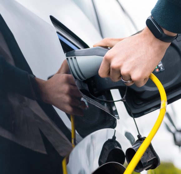 Man plugging in charger into an electric car at charge station