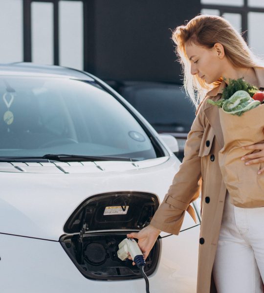 Woman with food shopping bags charging electric car